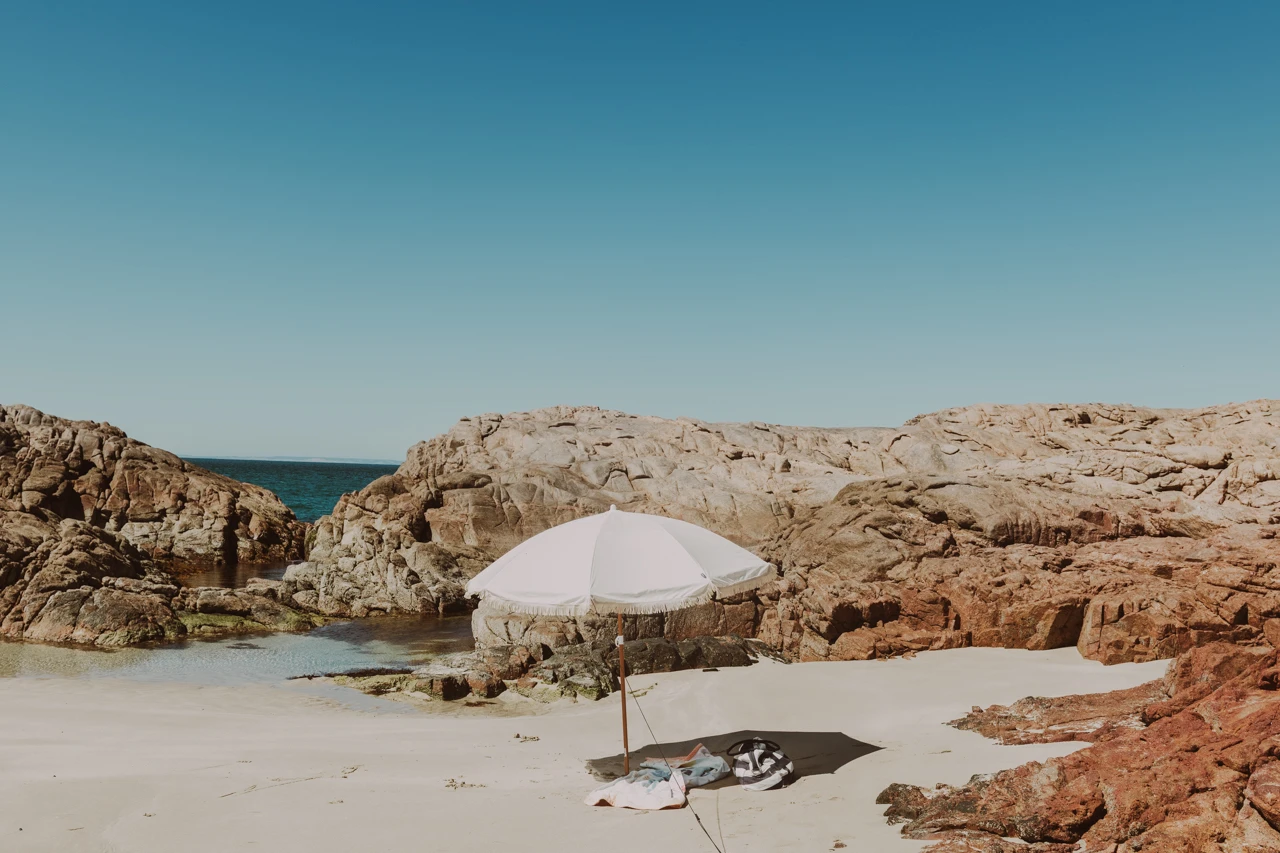Finding shelter in the rocks, sun umbrella and bag on sand Sun umbrella on the sand with rocks surrounding Vintage effect