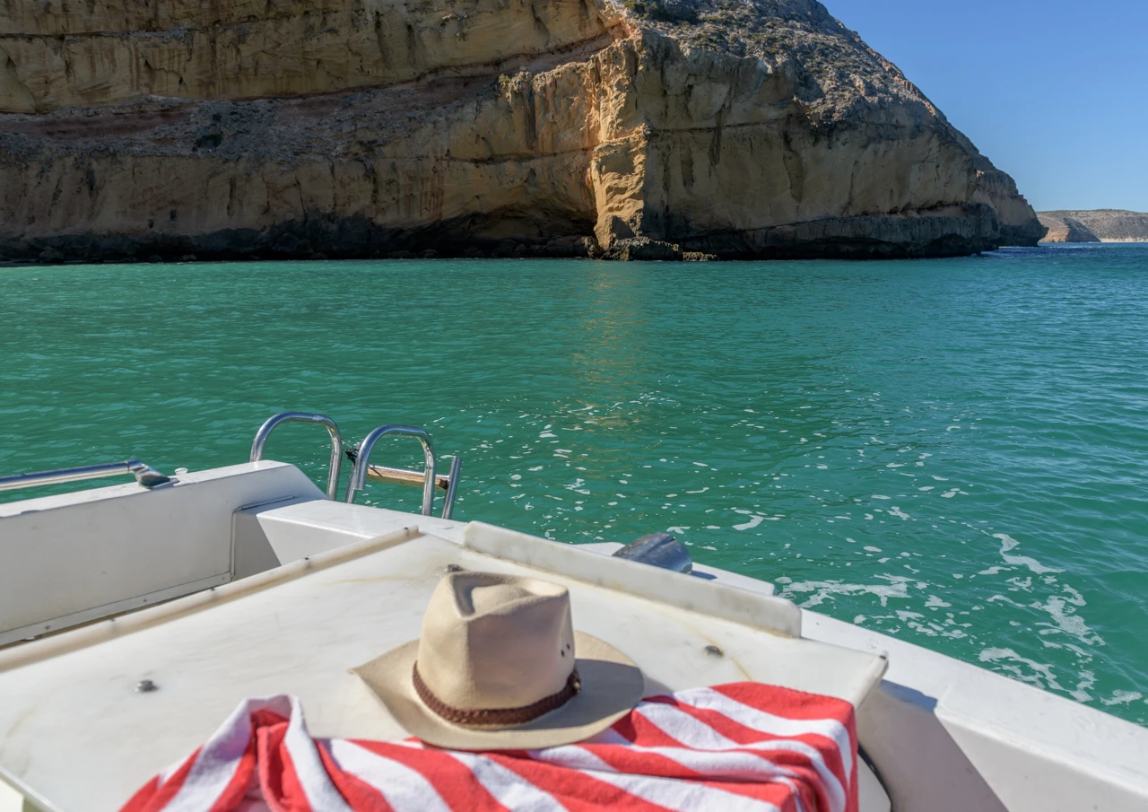 Red striped towel on the front of the boat, cliffs in distance.