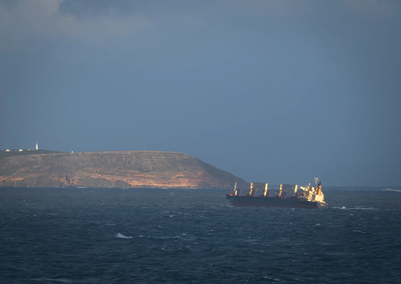 Ship passing close to shore buffeted by wind and big swell